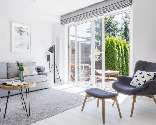 Armchair with patterned pillow and stool in living room interior with grey sofa and posters. Real photo